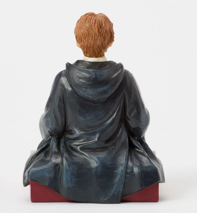 Back of figurine of Ron Weasley in a robe holding a rat, sitting on a box with Gryffindor emblem.