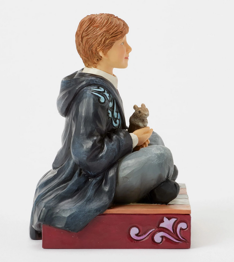 Ride side of figurine of Ron Weasley in a robe holding a rat, sitting on a box with Gryffindor emblem.