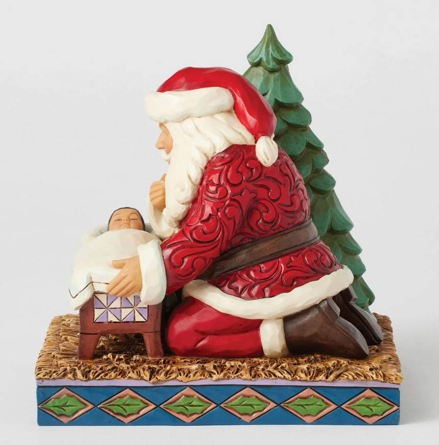 Front of Santa Claus figurine looking at a baby in a manger with a Christmas tree on a white background