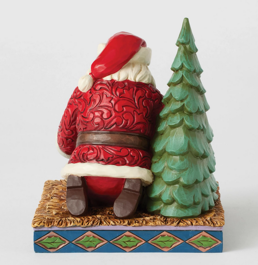 Back of Santa Claus figurine looking at a baby in a manger with a Christmas tree on a white background