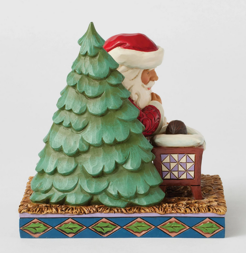 Side of Santa Claus figurine looking at a baby in a manger with a Christmas tree on a white background