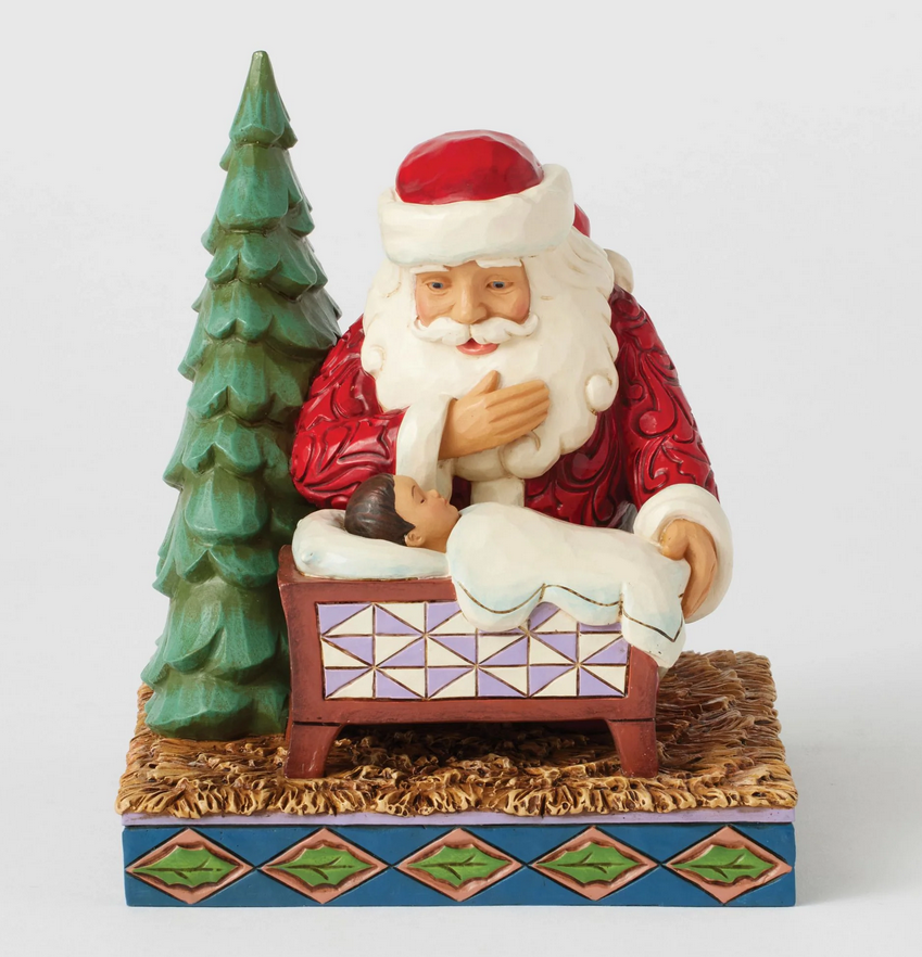 Side of Santa Claus figurine looking at a baby in a manger with a Christmas tree on a white background
