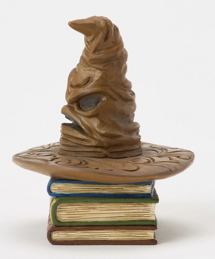 left side of figurine of a Sorting Hat on top of books with decorative covers on a white background