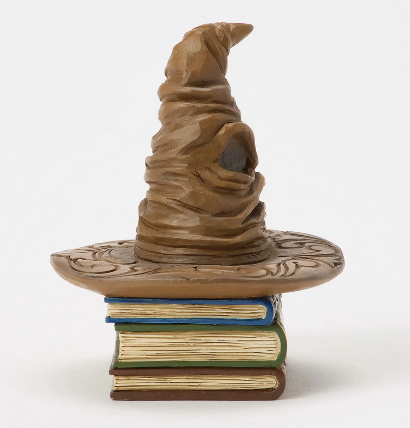 Ride side of figurine of a Sorting Hat on top of books with decorative covers on a white background