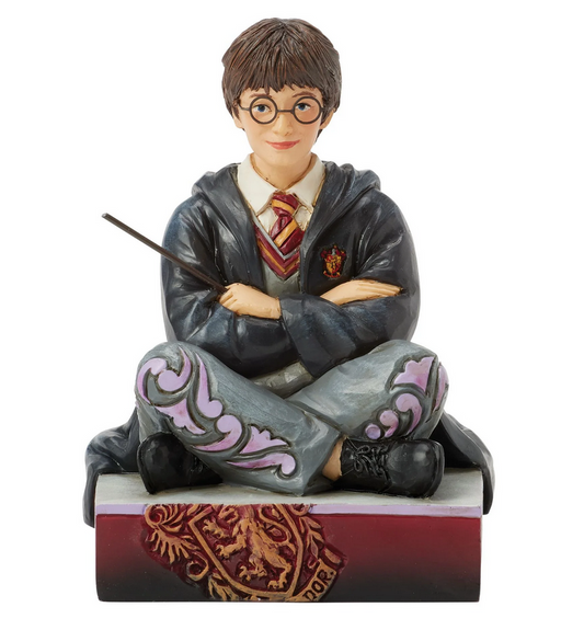 Figurine of Harry Potter in a gray robe with a wand, sitting on a red and gold box.