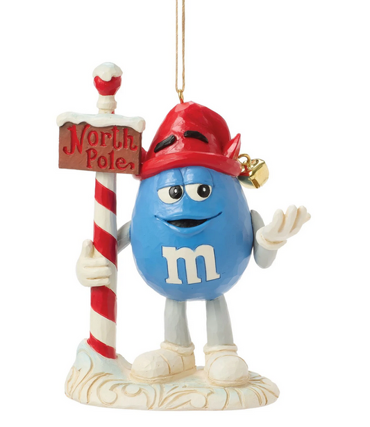 Front Blue M&M character ornament in a Santa hat holding a North Pole sign, on a white background