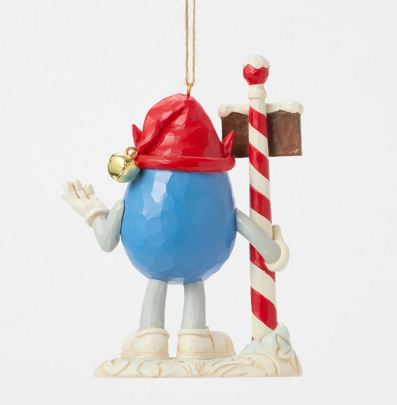Back of decorative ornament of a blue M&M character with a red hat holding a candy cane sign on a white background