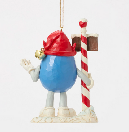 Back of decorative ornament of a blue M&M character with a red hat holding a candy cane sign on a white background