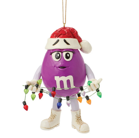 Purple M&M character ornament wearing a Santa hat holding Christmas lights on a white background