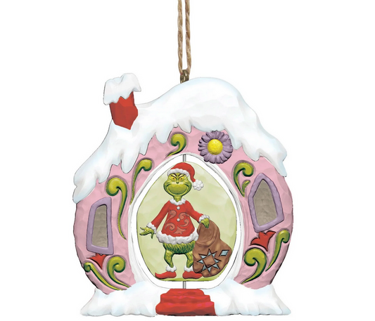 Decorative Christmas ornament featuring the Grinch in a pink house with snow on the roof.