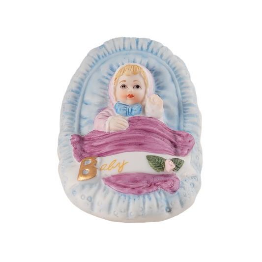 Decorative figurine of a baby in a blue crib with 'Baby' written on it.