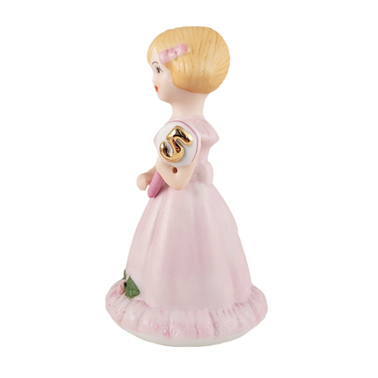 Side of figurine of a girl in a pink dress with a gold emblem on a white background