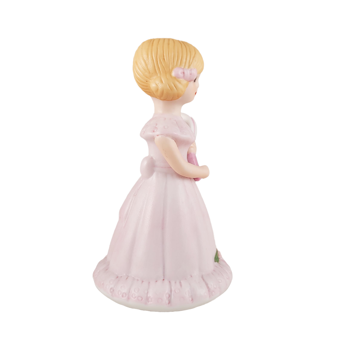 Side of figurine of a girl in a pink dress with a gold emblem on a white background