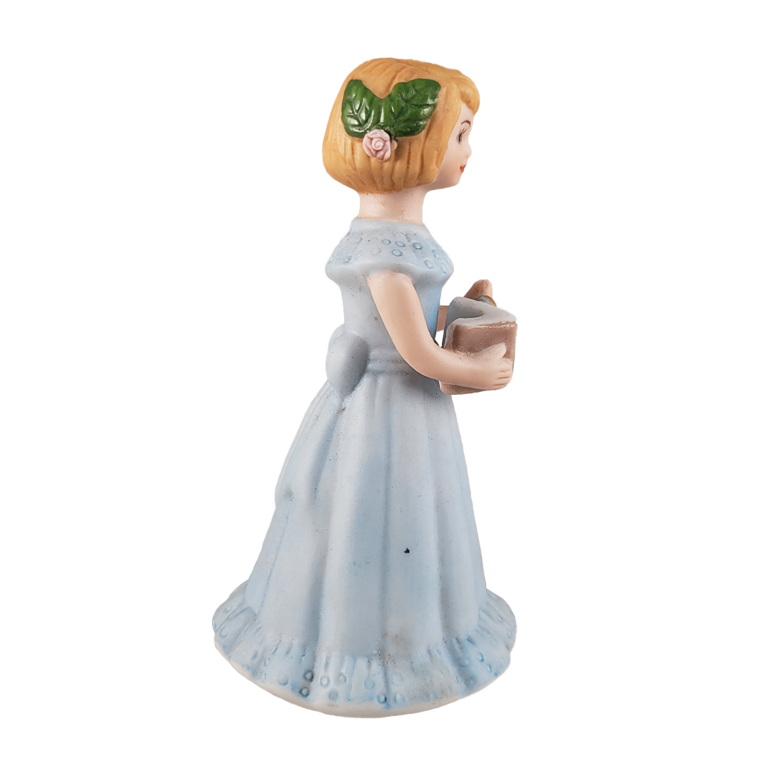 Side of figurine of a girl in a light blue dress holding a book on a background