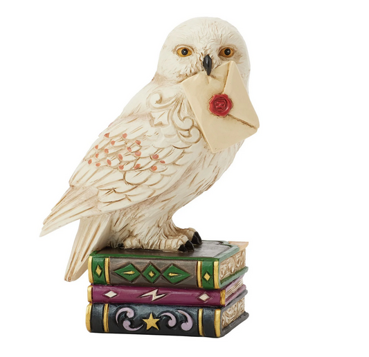 Front of figurine of the owl, Hedwig, with a letter on top of books against a white background