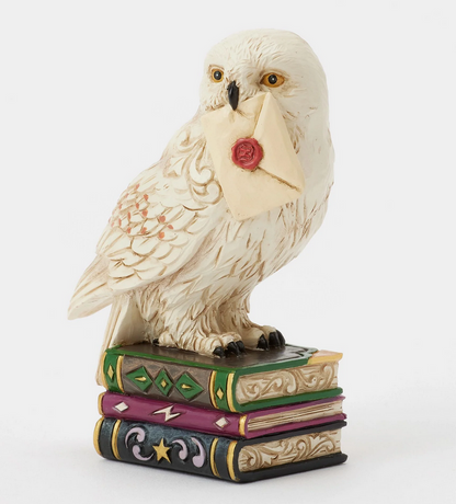 Quarter view of figurine of the owl, Hedwig, with a letter on top of books against a white background