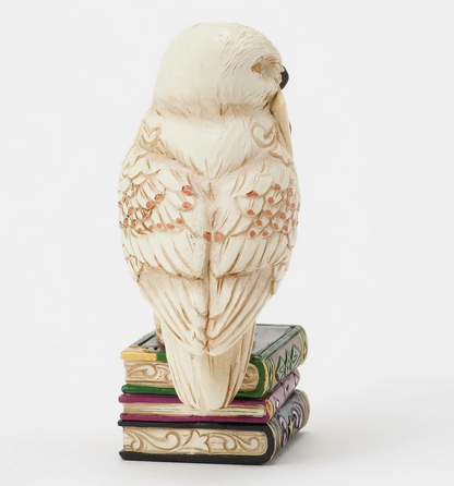 Right side of figurine of the owl, Hedwig, with a letter on top of books against a white background
