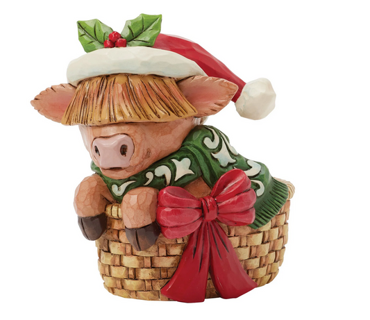 Decorative highland cow figurine with a Santa hat, green scarf, and in a basket on a white background