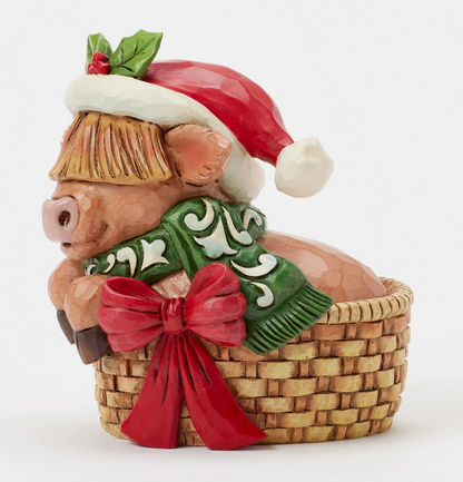 Side of decorative highland cow figurine with a Santa hat, green scarf, in a basket on a white background