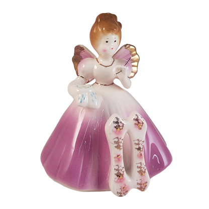 front of angel figurine hold a needle and cloth wearing a purple dress and a number 11 on a white background