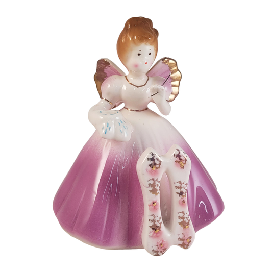 front of angel figurine hold a needle and cloth wearing a purple dress and a number 11 on a white background