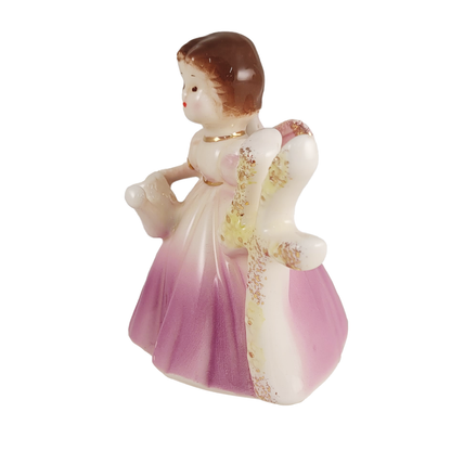 Side of small angel figurine in a pink dress holding a number 4 and teapot on a white background.