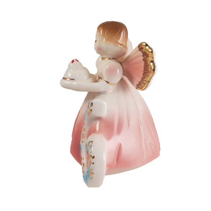 Side of porcelain angel figurine with a pink dress and gold wings holding a cake on a white background