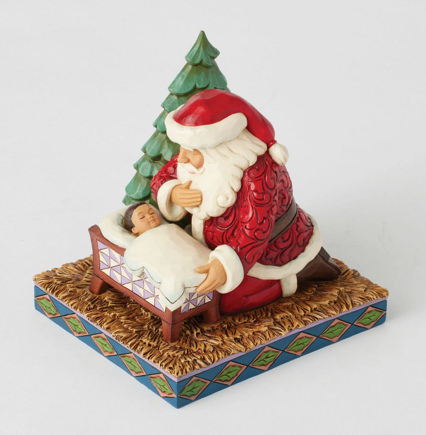 Lookin down on Santa Claus figurine looking at a baby in a manger with a Christmas tree on a white background