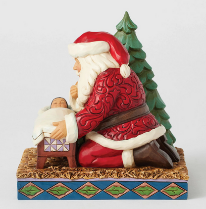Front of Santa Claus figurine looking at a baby in a manger with a Christmas tree on a white background