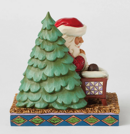 Side of Santa Claus figurine looking at a baby in a manger with a Christmas tree on a white background