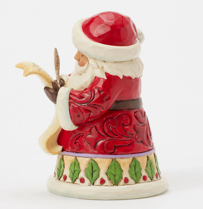 Left side of Santa Claus figurine holding a feather and quill on a white background