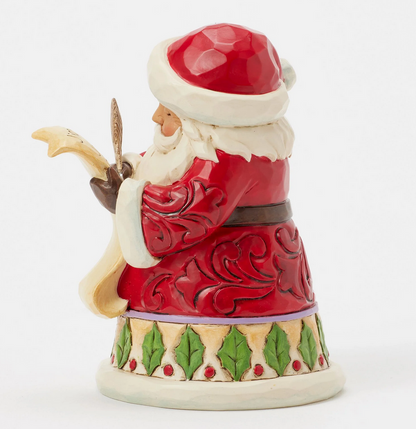 Left side of Santa Claus figurine holding a feather and quill on a white background